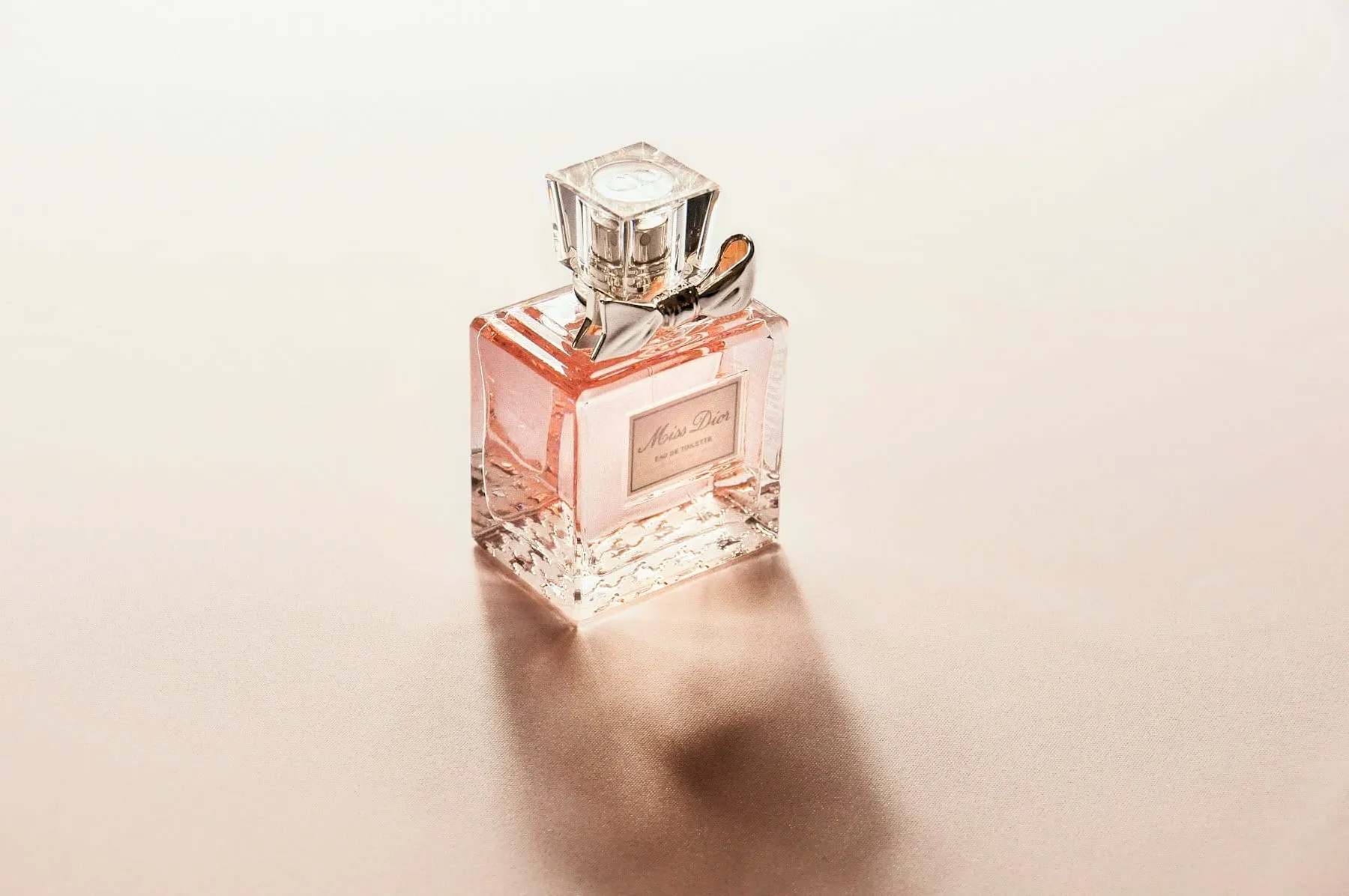 A pale pink perfume bottle casting a long studio shadow