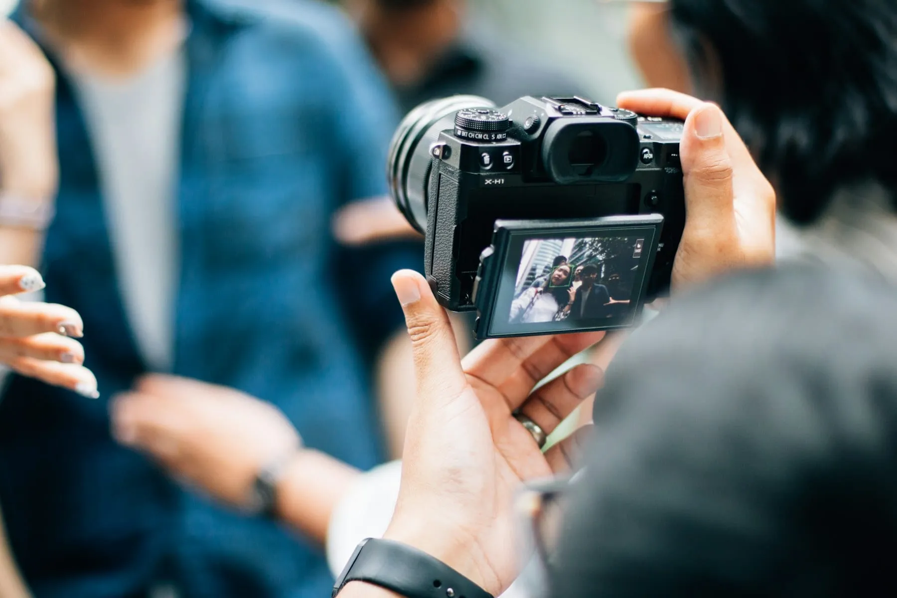A photographer holding a camera with a candid street scene on the screen