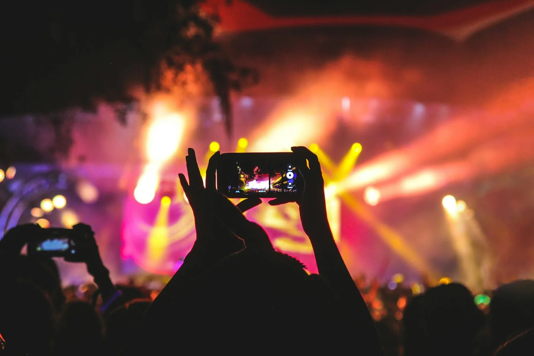 A phone recording a bright concert stage with pink and yellow lights