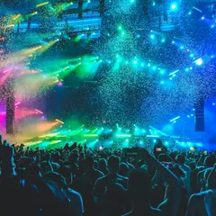 A packed concert crowd under blue, green, and pink confetti lights
