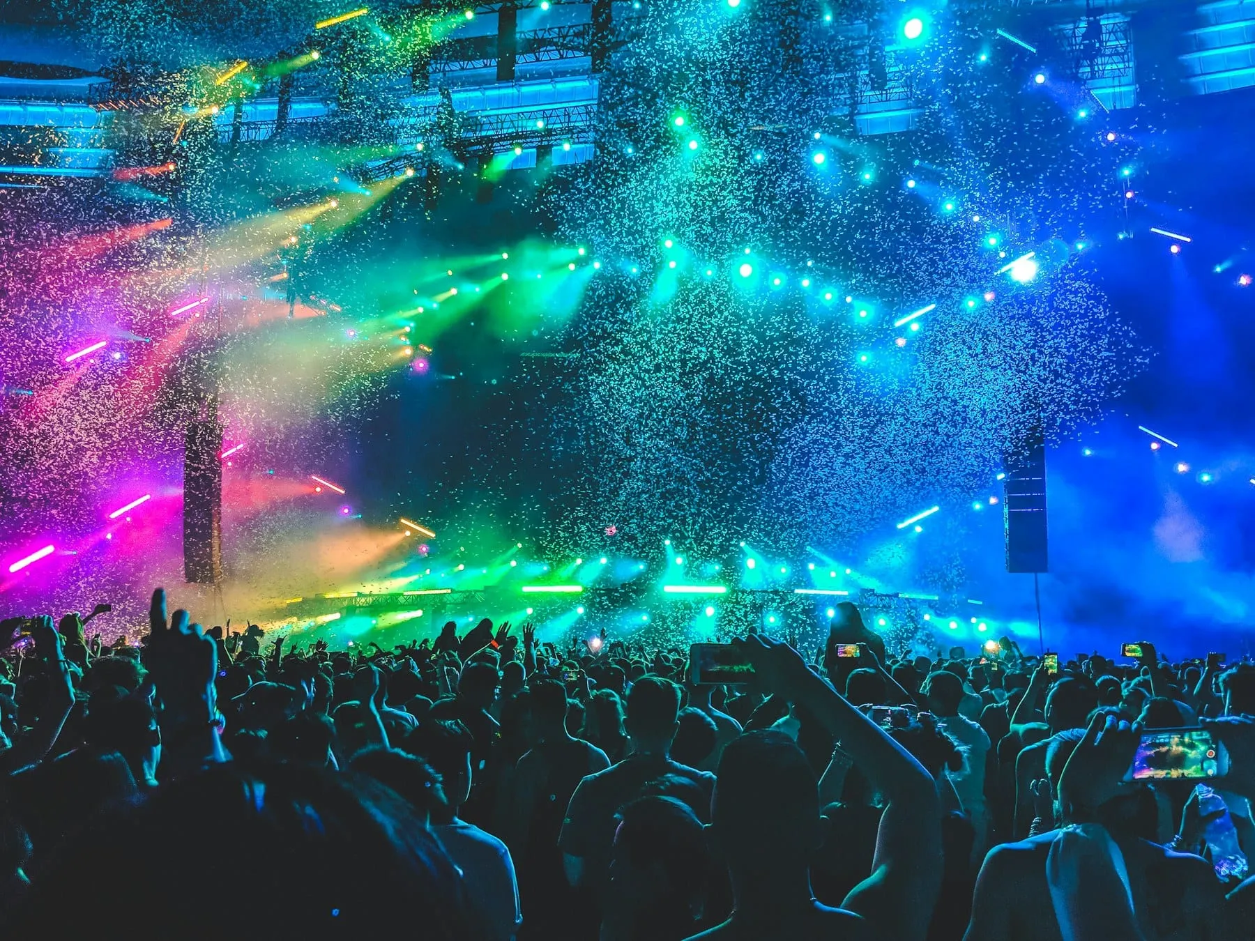 A packed concert crowd under blue, green, and pink confetti lights