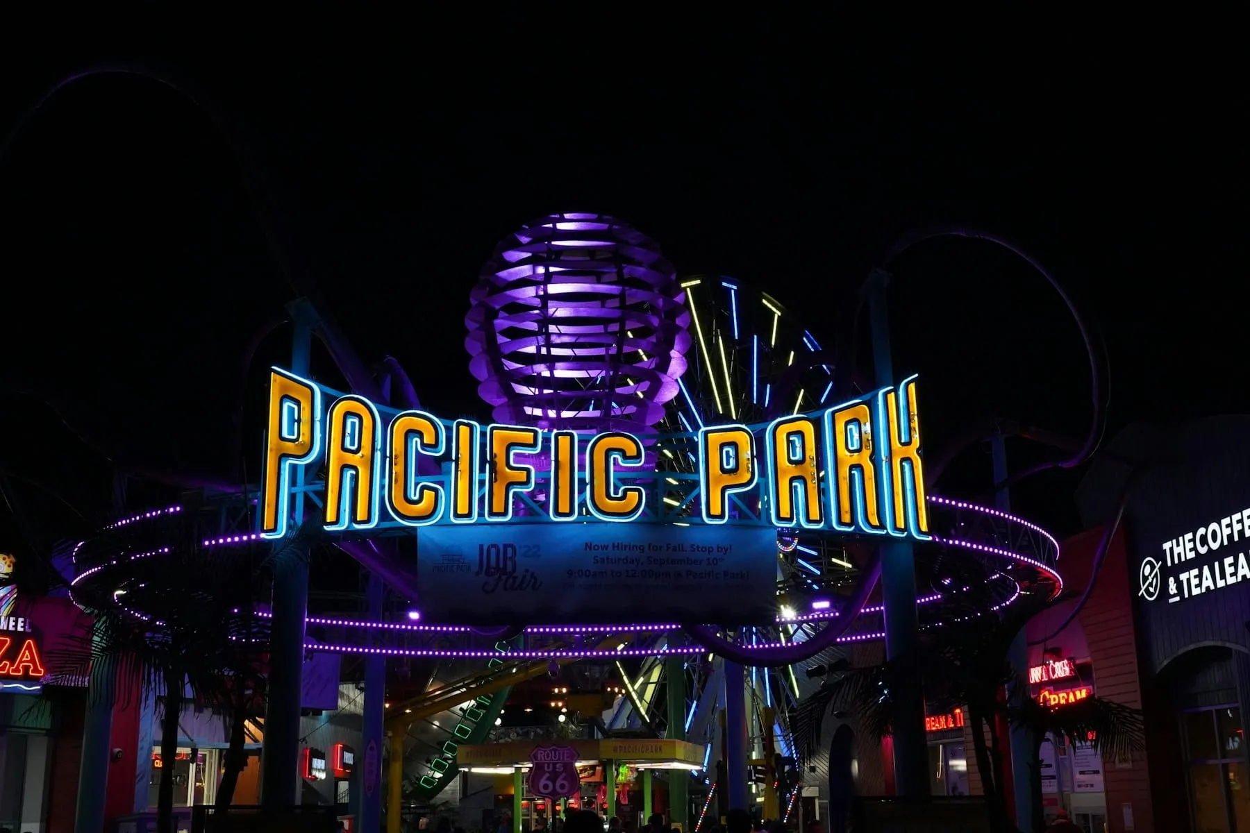 A neon sign glowing at night with a ferris wheel in the background