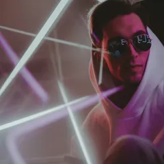 A woman in black sunglasses and a purple hoodie posing against a grey backdrop