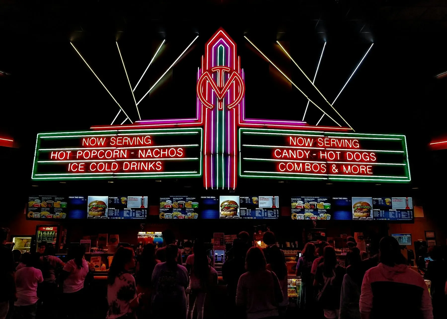 A neon cinema concession sign glowing over a busy counter