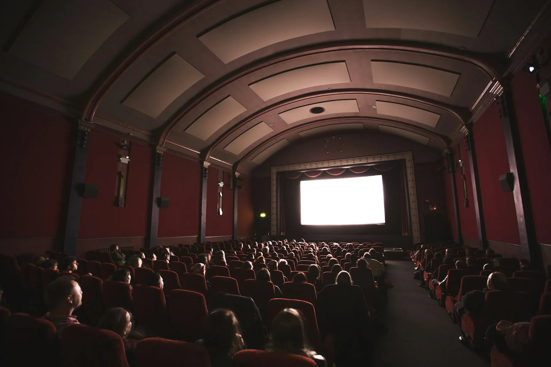 A full movie theater watching a bright screen from red seats