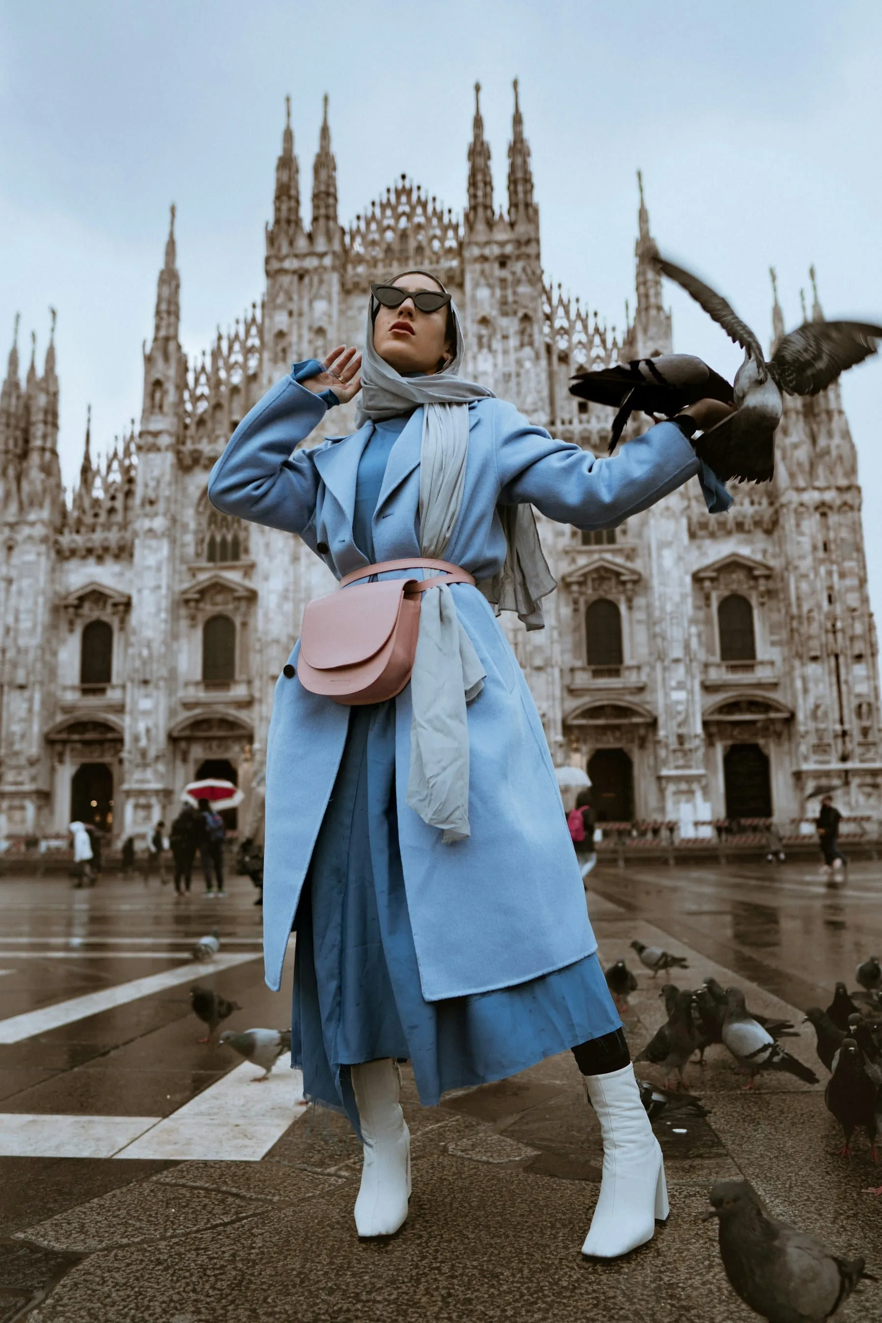 A fashion guest in a blue coat posing outside a cathedral
