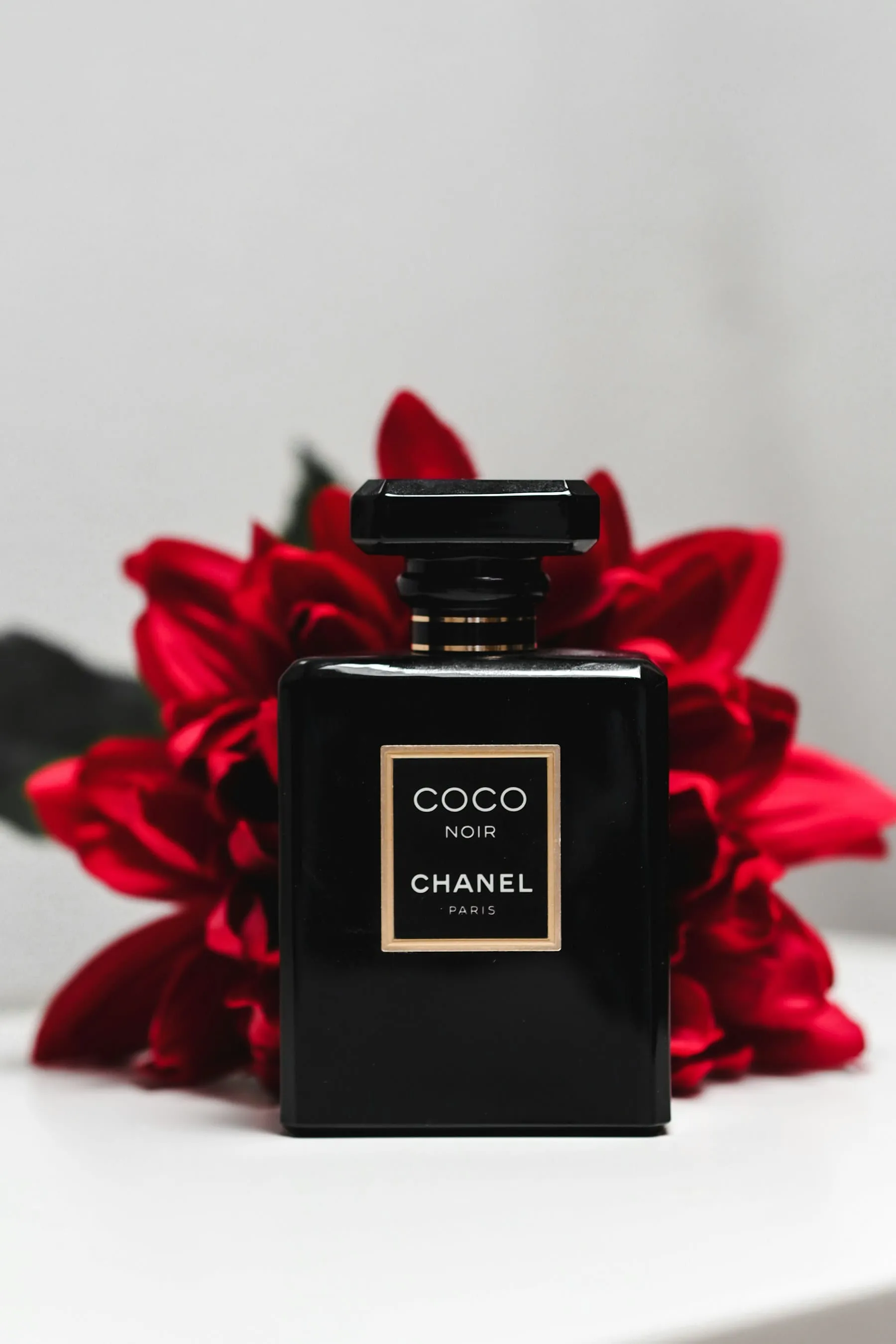 A black perfume bottle framed by vivid red petals